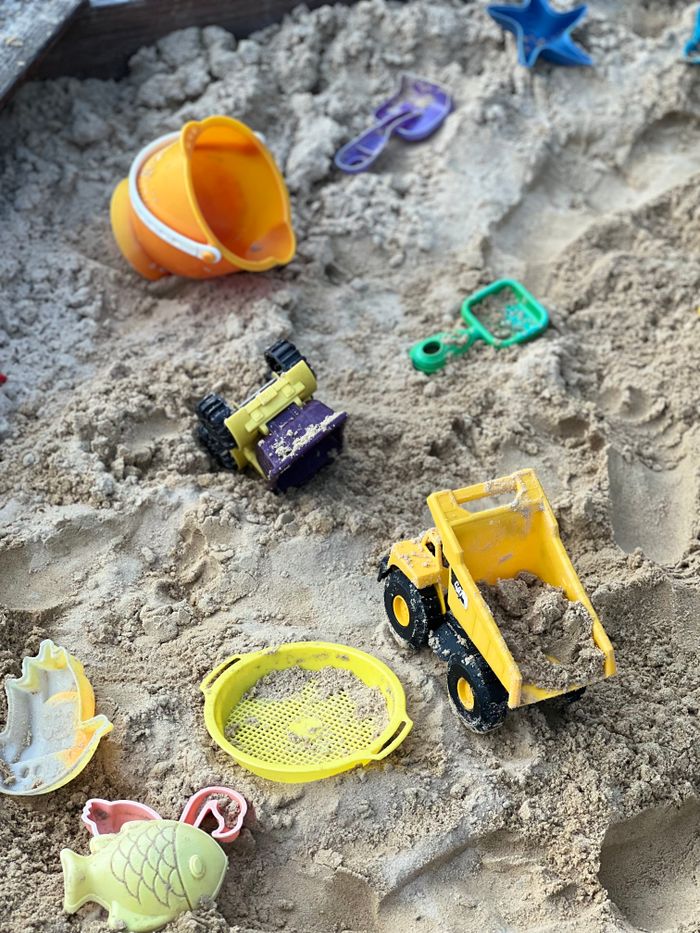 Vibrant plastic toys scattered in a sandy playground sandbox.